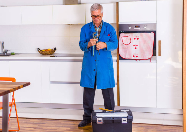 Старый ремонтник стоит на кухне возле ящика с инструментами.
 - Фото, изображение