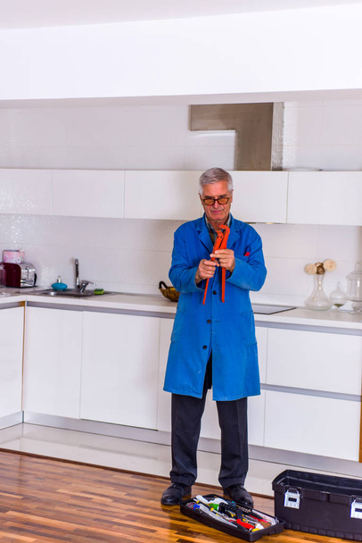 Kypsä yleismies seisoo keittiössä työkalupakin lähellä ja näyttää onnelliselta
 - Valokuva, kuva