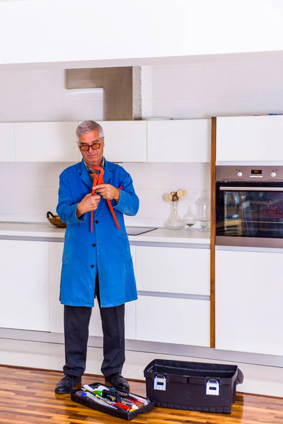 Серйозний чоловік ремонтант тримає пальники і працює всередині кухні біля коробки інструментів
 - Фото, зображення