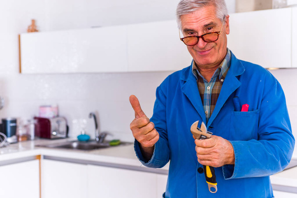 Handyman está sorrindo e olhando satisfeito enquanto trabalhava na cozinha e mostra polegares para cima
 - Foto, Imagem