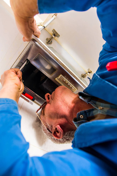 Ein Arbeiter im blauen Arbeitsanzug befestigt die Dunstabzugshaube in der Küche - Foto, Bild
