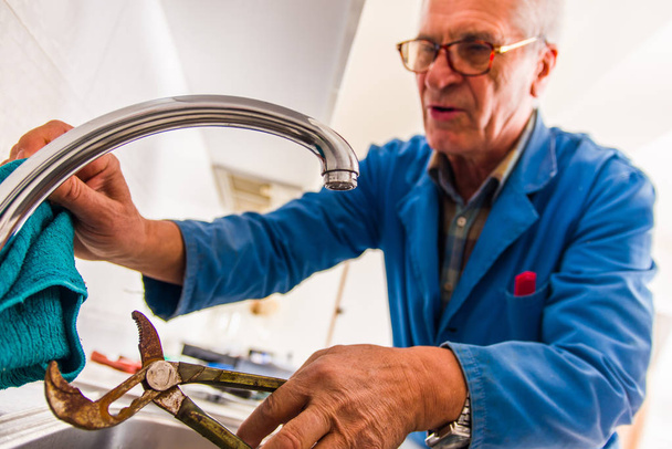 O faz-tudo profissional está consertando a torneira da cozinha com seus pilers
 - Foto, Imagem