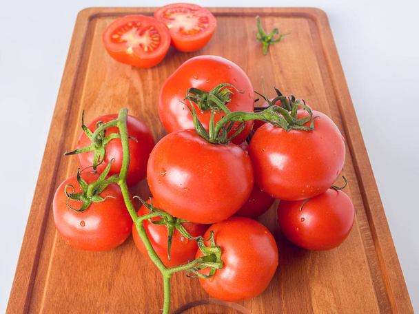 Red ripe tomato branch on a brown wooden cutting board on a neutral background. Healthy eating and vegetarian food concept, close up, selective focus. - Foto, Bild
