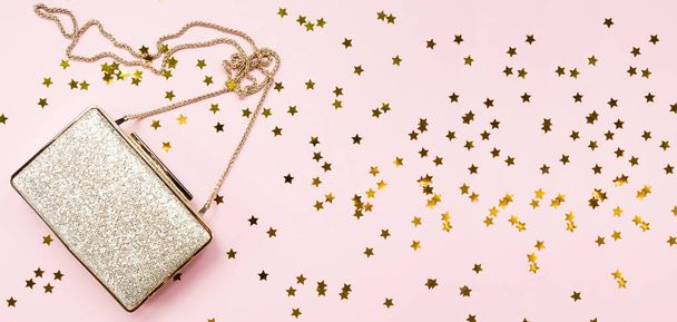 Festive evening golden clutch with star sprinkles on pink. Holiday and celebration background. Luxury accessories and party concept. Horizontal, wide screen banner format - Foto, afbeelding
