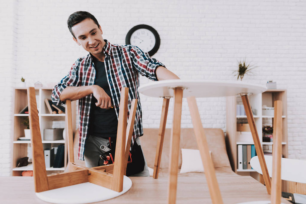 Young Man Assembling Coffee Table and Stools. Furniture Fittings. Engineer with Tool. Young Man at Home. Wooden Coffee Table. Selfmade Furniture. Man and Hobby. White Table in Room. - Foto, imagen