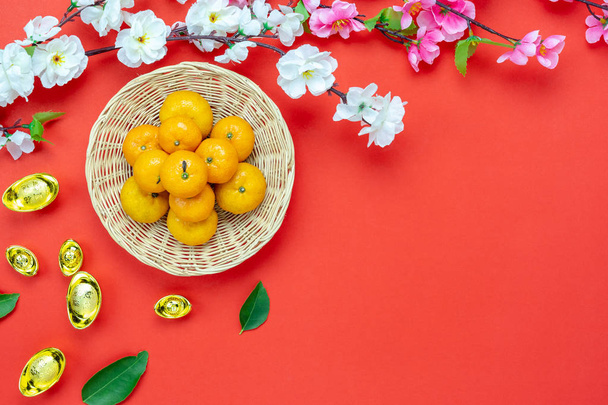 Top view aerial image shot of arrangement decoration Chinese new year & lunar new year holiday background concept.Flat lay fresh orange in basket & gold money with blossom on modern red wooden. - Фото, зображення