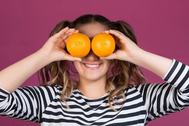 Portret van een vrolijke jonge meisje houdt twee sinaasappelen op haar gezicht op roze achtergrond - Foto, afbeelding