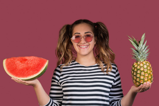 カラフルなピンク背景にパイナップルと watermeloni のスライスを保持しているサングラスのファッション ポートレート クールな女の子。健康食品のコンセプト - 写真・画像