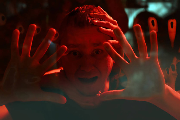 Las manos extendidas al hombre detrás del cristal sobre el fondo rojo sangriento. Atentado de pánico
 - Foto, imagen