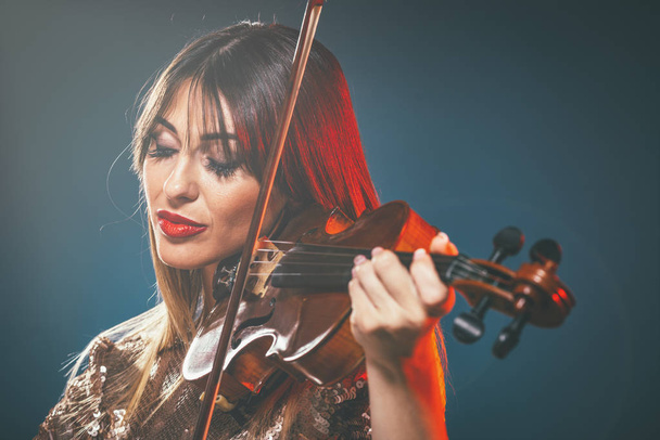mujer joven en vestido de lentejuelas tocando música clásica en violín
 - Foto, Imagen
