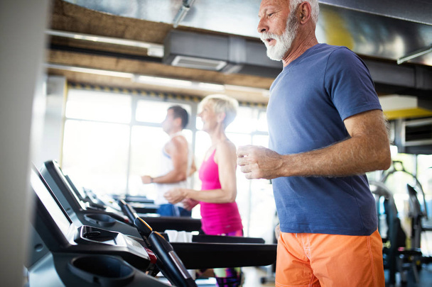 Happy mature people running together on treadmills in gym. - Fotoğraf, Görsel