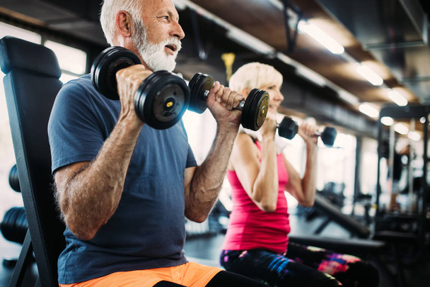 Mature fit man and woman doing exercises in gym to stay healthy - Photo, image