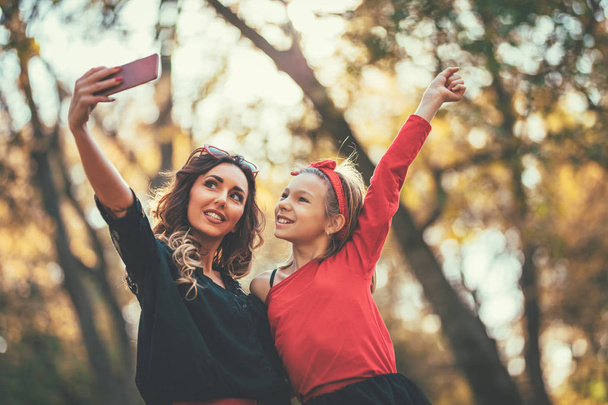 young mother and daughter taking selfie in autumn forest at sunset - Fotoğraf, Görsel