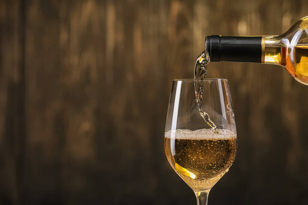 Versare il vino bianco dalla bottiglia in bicchiere su fondo scuro
 - Foto, immagini