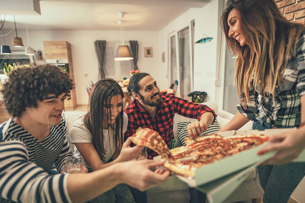 Grupo de amigos alegres divirtiéndose y comiendo pizza en casa
 - Foto, Imagen
