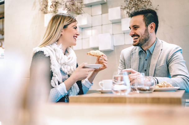 Νεαρό ζευγάρι πίνει καφέ και τρώει κρουασάν σε καφετέρια - Φωτογραφία, εικόνα
