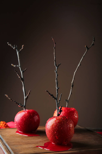Delicious caramel apples with tree branches on wooden board - Фото, изображение