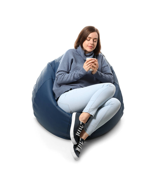 Young woman with cup of tea sitting on beanbag chair against white background - Photo, Image