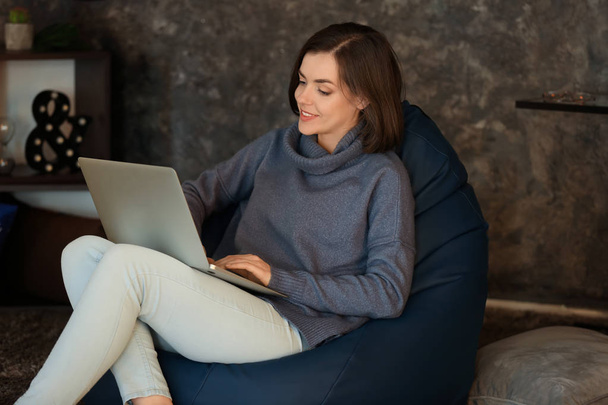 Young woman with laptop sitting on beanbag chair at home - Foto, Imagen