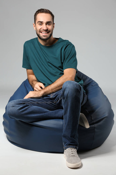 Młody mężczyzna siedzi na krześle beanbag na szarym tle - Zdjęcie, obraz