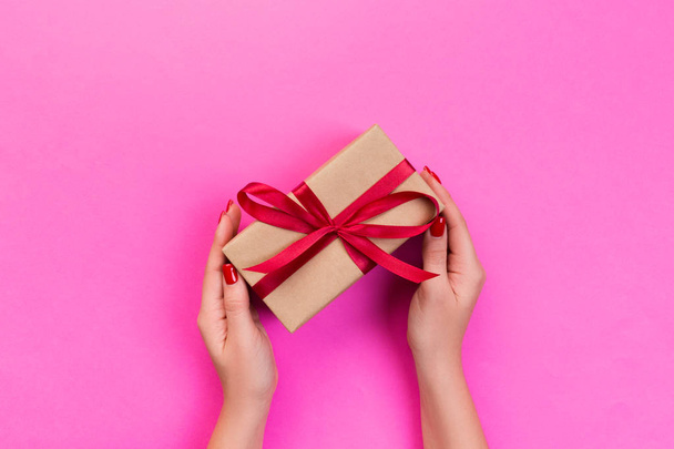 Frauenhände schenken eingewickelten Valentin oder andere handgemachte Geschenke in Papier mit roter Schleife. Geschenkbox, Geschenkdekoration auf rosa Tisch, Draufsicht mit Kopierraum. - Foto, Bild