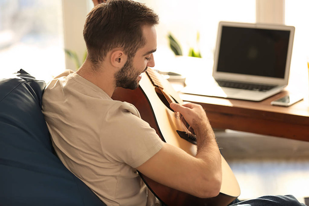 Jeune homme avec guitare assis sur une chaise de haricot à la maison
 - Photo, image
