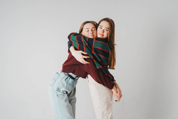 Dwie siostry bliźniaczki piękne dziewczyny biodrówki w odzieży casual na szare tło na białym tle, pojęcie miłości, przyjaźni, bratnie dusze - Zdjęcie, obraz