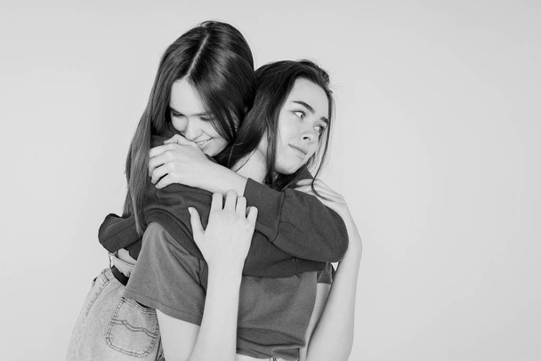 Dvě sestry dvojčata bokovky krásné dívky v neformálním oblečení na šedé pozadí, samostatný pojem láska, přátelství, spřízněné duše - Fotografie, Obrázek