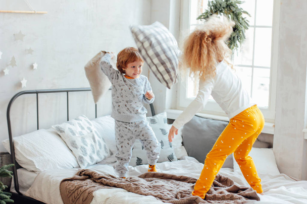 Брат и сестра в пижаме играют с подушками на кровати
 - Фото, изображение