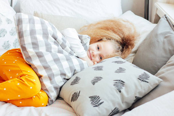 Little beautiful curly blonde girl woke up and smiling, cozy morning - Foto, Imagem