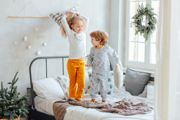 Brother and sister in pajamas playing with pillows on the bed, christmas morning - Foto, Bild