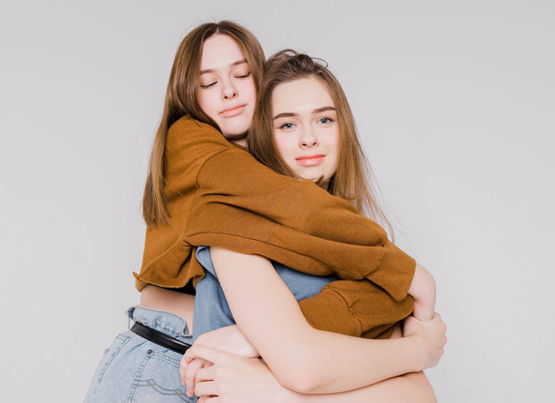 Two sisters twins beautiful girls hipsters in casual clothing on grey background isolated, concept love, friendship, soul mates - Fotoğraf, Görsel