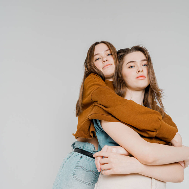 zwei Schwestern Zwillinge schöne Mädchen Hipster in lässiger Kleidung auf grauem Hintergrund isoliert, Konzept Liebe, Freundschaft, Seelenverwandte - Foto, Bild