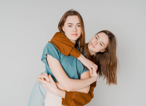 Two sisters twins beautiful girls hipsters in casual clothing on grey background isolated, concept love, friendship, soul mates - Zdjęcie, obraz