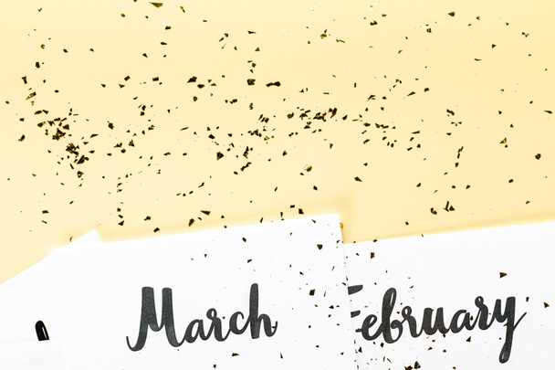 Draufsicht auf März- und Februar-Kalender und goldenes Konfetti auf beigem Hintergrund  - Foto, Bild