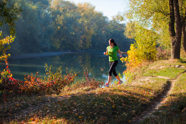 Jogging woman on the autumn pond and forest background - Foto, imagen