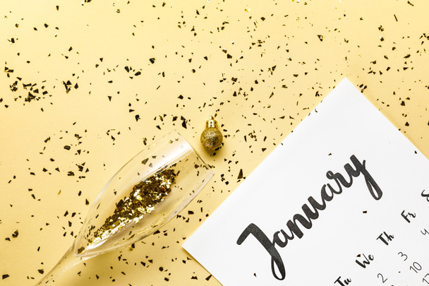 top view of january calendar, christmas bauble and glass with golden confetti on beige  - Foto, immagini