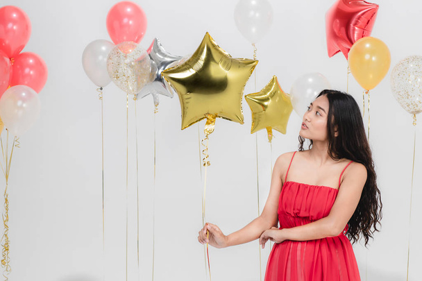 Mooie jonge Aziatische vrouw in rode jurk, gelukkig lachend op leuke partij terwijl de kleurrijke ballonnen. Studio portret shot op witte achtergrond. - Foto, afbeelding