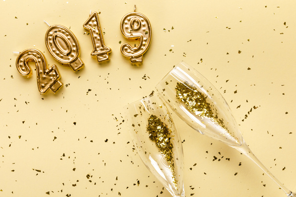 top view of champagne glasses with golden confetti and 2019 candles on beige - Foto, imagen