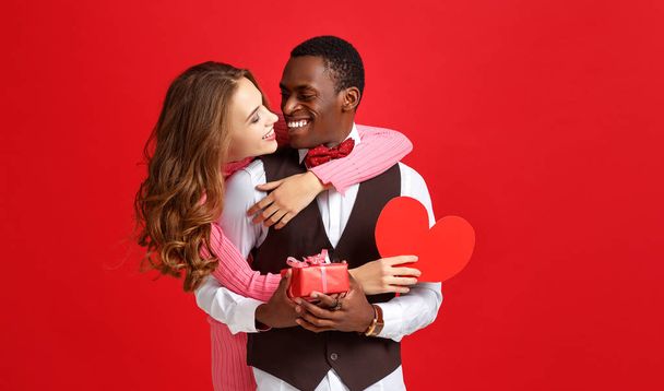 Valentinstag-Konzept. glückliches junges Paar mit Herz, Blumen, Geschenk auf rotem Hintergrund - Foto, Bild
