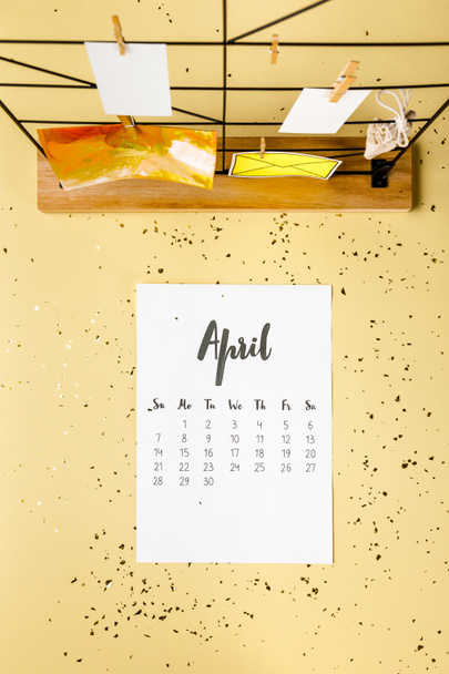 top view of april calendar with golden confetti and cards with clothespins on beige - Foto, immagini