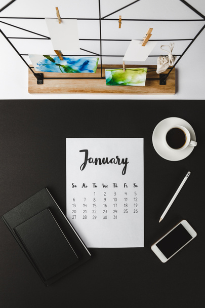 felülnézet január naptár, jegyzetfüzet, smartphone és kávét a munkahelyen  - Fotó, kép