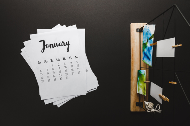 top view of january calendar and paintings on clothespins on black - Foto, afbeelding