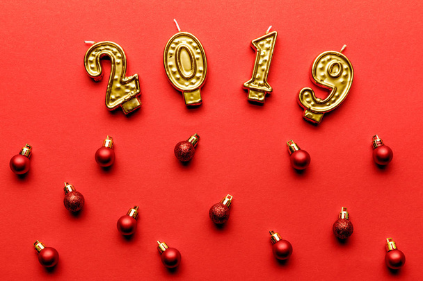 bovenaanzicht van gouden 2019 kaarsen en rode kerstballen op rood   - Foto, afbeelding