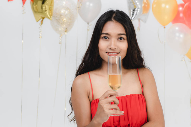 Attractive young asian woman in red dress has drink in her hands be happy at fun party, portrait on white background with colorful festive balloons. - Photo, image