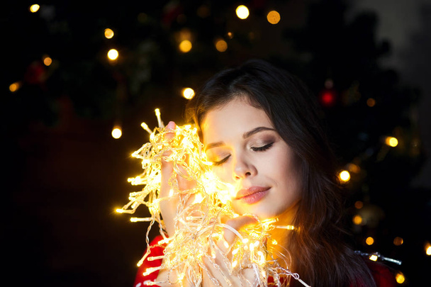 Beautiful young woman smiling and talking garlands of lights at home - Fotoğraf, Görsel