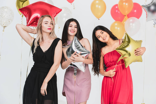 Różnorodność młodych kobiet szczęśliwy i zabawy razem w partii, tło białe i kolorowe balony uroczysty. - Zdjęcie, obraz