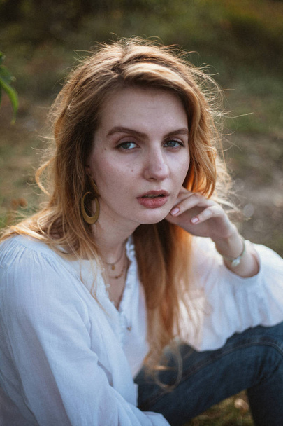 sensual woman in white linen blouse and jeans looking at camera while siting on meadow  - Foto, Imagen
