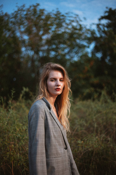 sensual woman in grey jacket looking at camera while posing at meadow at sunny day  - Fotografie, Obrázek