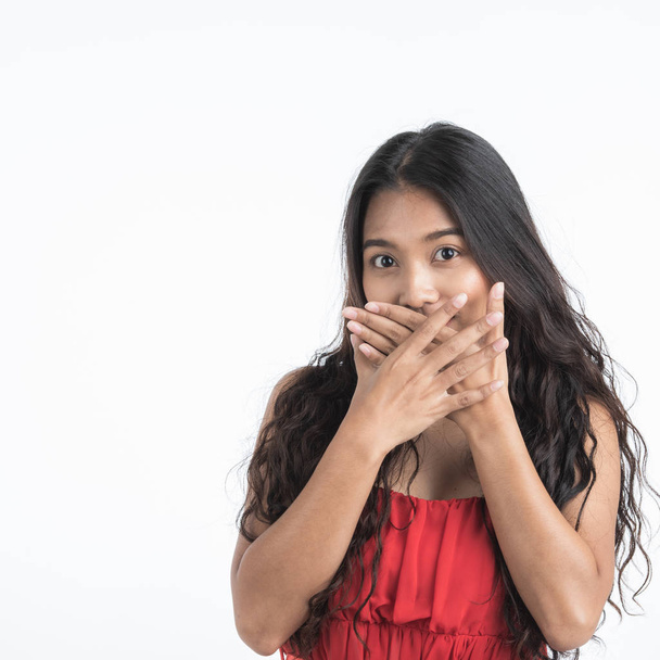 Beautiful young woman in red dress put hands covering her mouth as secret sign concept, portrait shot isolated on white background. - Foto, Bild